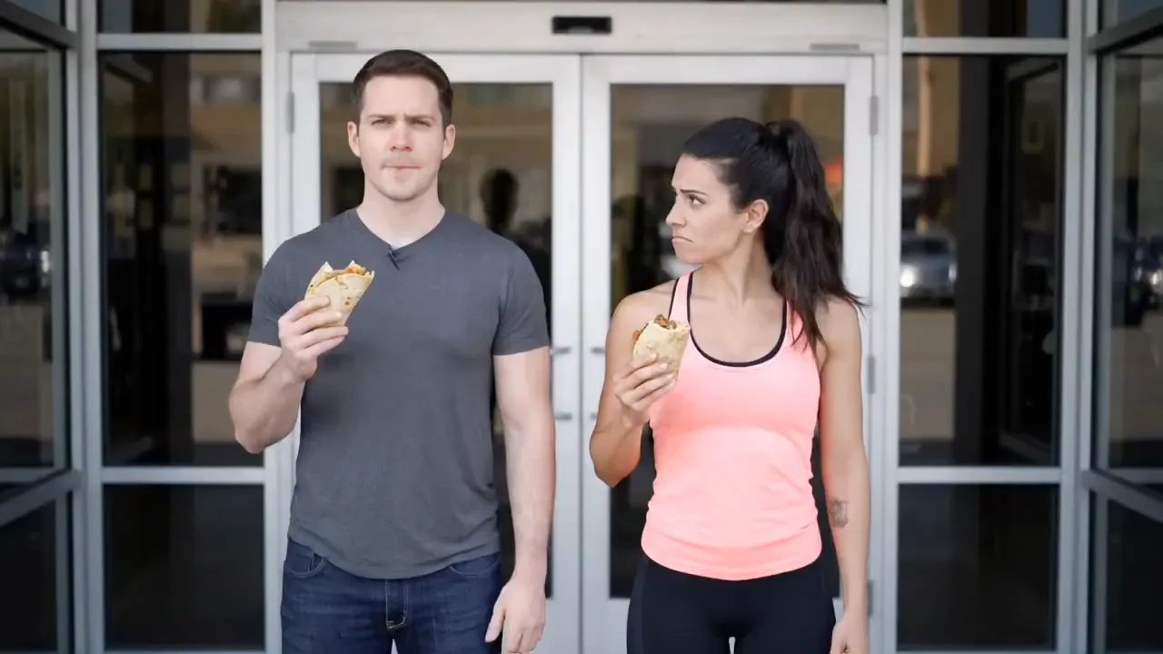 Two people stand in front of a gym entrance with tacos
